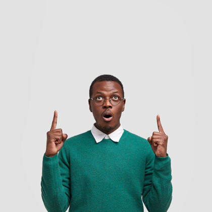 广告照片中惊讶的黑人年轻人用食指指着天花板 惊讶地张嘴向上指示服装