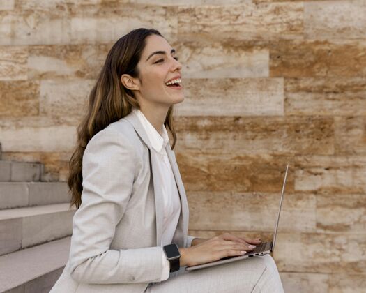 专业人士smileybusinesswoman侧视图 智能手表在户外笔记本电脑上工作女商人个人笔记本电脑