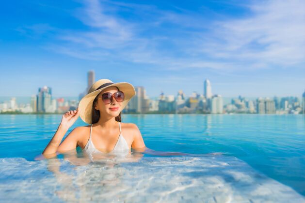 高肖像美丽的亚洲年轻女子微笑放松休闲围绕室外游泳池与城市景观女性梦想中心
