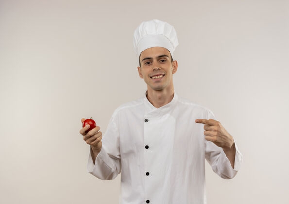 制服身着厨师制服的年轻男厨师微笑着指着手中的西红柿手指男穿