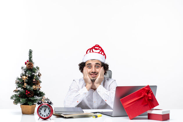 电脑忙碌的年轻商人戴着滑稽的圣诞老人帽子 在白色背景的办公室里摆姿势拍照专业帽子办公室