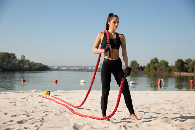 户外年轻健康的女人在沙滩上摆弄着绳索肌肉户外身体
