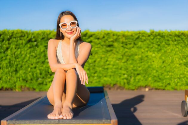 享受美丽的亚洲年轻女子在度假酒店的室外游泳池周围放松的肖像热带泳装放松
