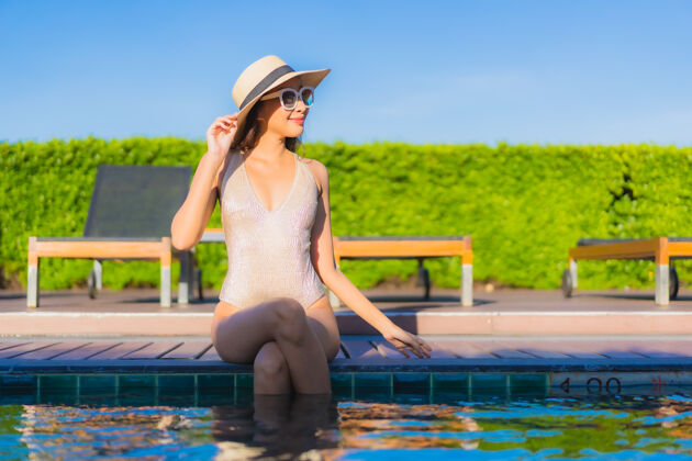 享受美丽的亚洲年轻女子在度假酒店的室外游泳池周围放松的肖像放松游泳水