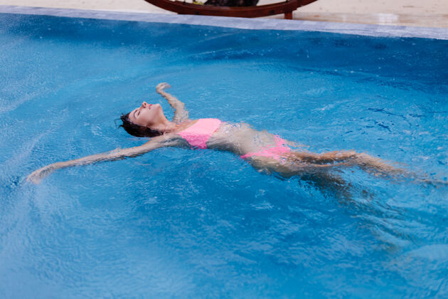 海滩在明亮的粉红色比基尼蓝色游泳池里的年轻快乐修长的欧洲女人性感游泳池女人