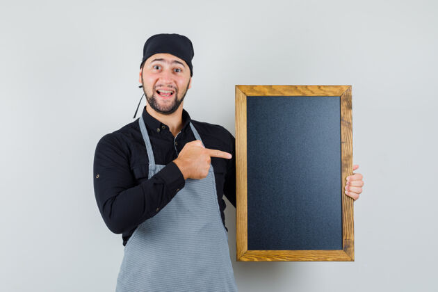 烹饪男厨师指着黑板 穿着衬衫 围裙 看上去很开心正面图烹饪人厨房