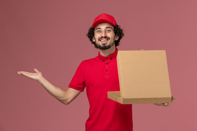 员工正面图穿着红色衬衫和披风的男信使拿着粉红色墙上的食品盒帽子人微笑