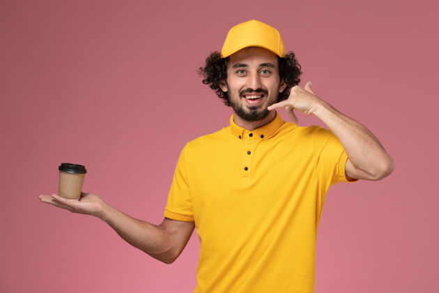 送货正面图：身穿黄色制服 披风的男性快递员手持粉色墙上的送货咖啡杯男男视图