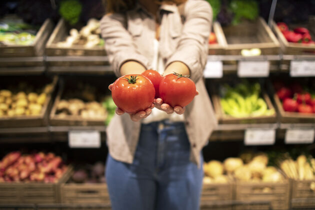 货架超市里手拿西红柿蔬菜的特写镜头销售成人满意