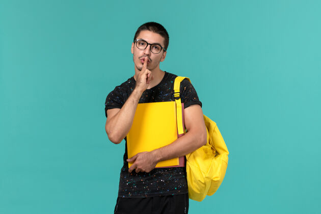 档案身穿深色t恤黄色背包的男学生正面图 浅蓝色墙上放着不同的文件模特男男学生