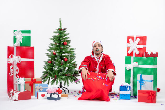 装饰圣诞老人坐在地上 玩弄圣诞装饰品 在礼物和白色背景上装饰圣诞树圣诞礼物人