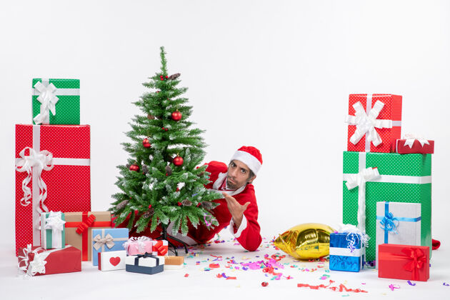 圣诞老人圣诞心情与年轻的圣诞老人躲在圣诞树附近的礼物在不同颜色的白色背景镜头礼物年轻圣诞