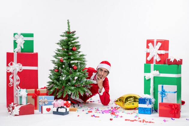圣诞圣诞心情与年轻的圣诞老人躲在圣诞树附近的礼物在不同颜色的白色背景图片不同圣诞老人季节性