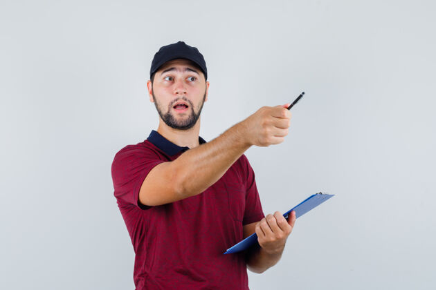 黑年轻的男性拿着笔记本和笔 穿着红色t恤 戴着黑色的帽子 看上去很小心 前视图小心钢笔肖像