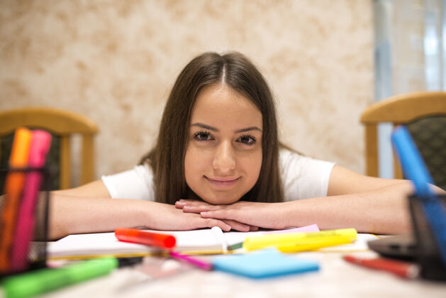 青少年满脸笑容的少女倚在桌子上 桌上摆满了铅笔 书和纸智力青少年任务