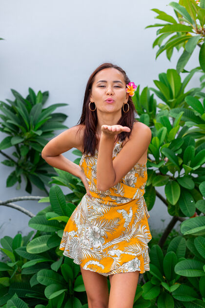 户外身着黄色夏装的亚洲女人的肖像站在那里 头发上插着泰国花 戴着圆耳环度假心情夏天