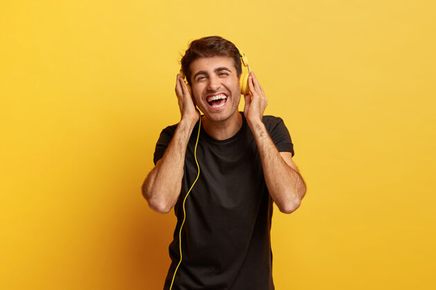 照片积极的人类情感和有趣的概念快乐快乐的白人男子双手戴着现代耳机 笑容灿烂拍摄男性耳机