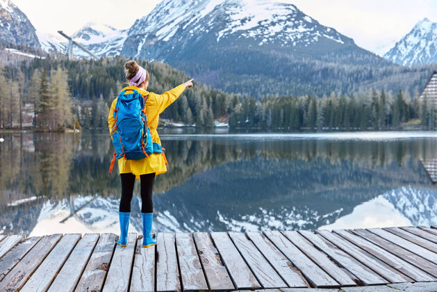 距离穿着黄色雨衣和蓝色胶靴的女游客站在山景前的水平镜头湖泊水平森林