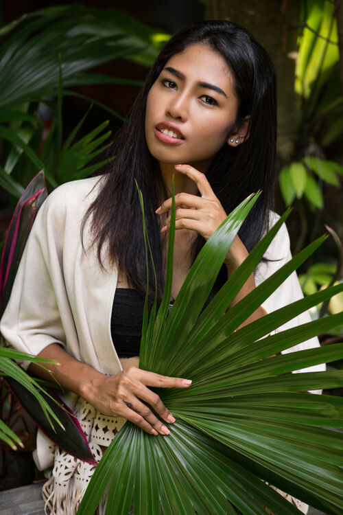 女人美丽的亚洲女人在热带花园里摆姿势 手里拿着大棕榈叶森林休闲度假