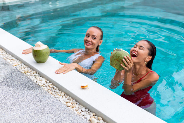 时尚两位亚洲人和白种人的女性朋友在别墅的游泳池化妆热带游泳池活跃