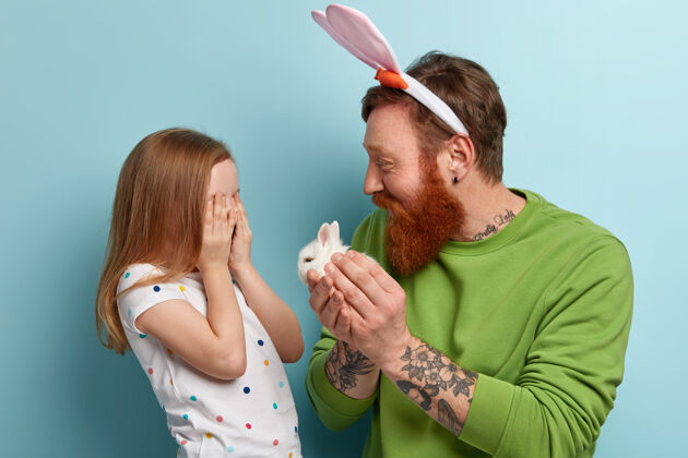 兔子姜黄胡子的男人穿着五颜六色的衣服 他的女儿抱着兔子人成人男性